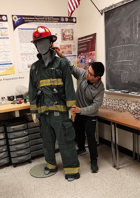 student stands in front of dummy dressed in firefighter gear