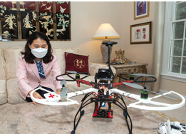 a woman sits in her home with the telehealth drone placed on a coffee table. 