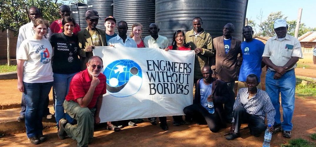 Engineers without Borders student organization Engineers without Borders-UC Chapter poses for a picture in Tanzania with locals. They are all helping to hold the Engineers without Borders sign.